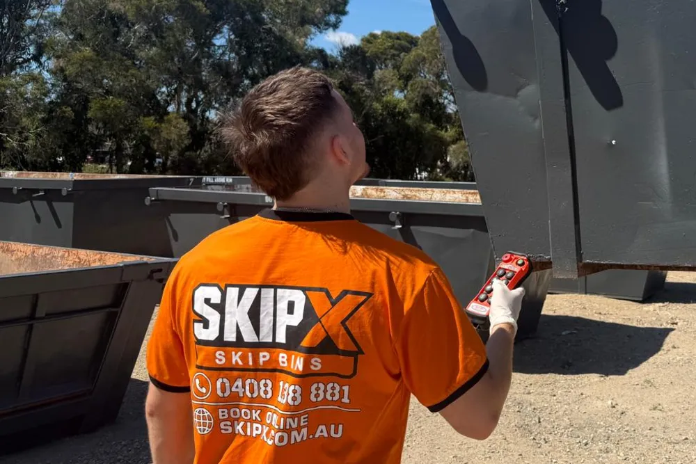 SKIP X driver in an orange SKIP X shirt lifting a skip bin with the truck's remote